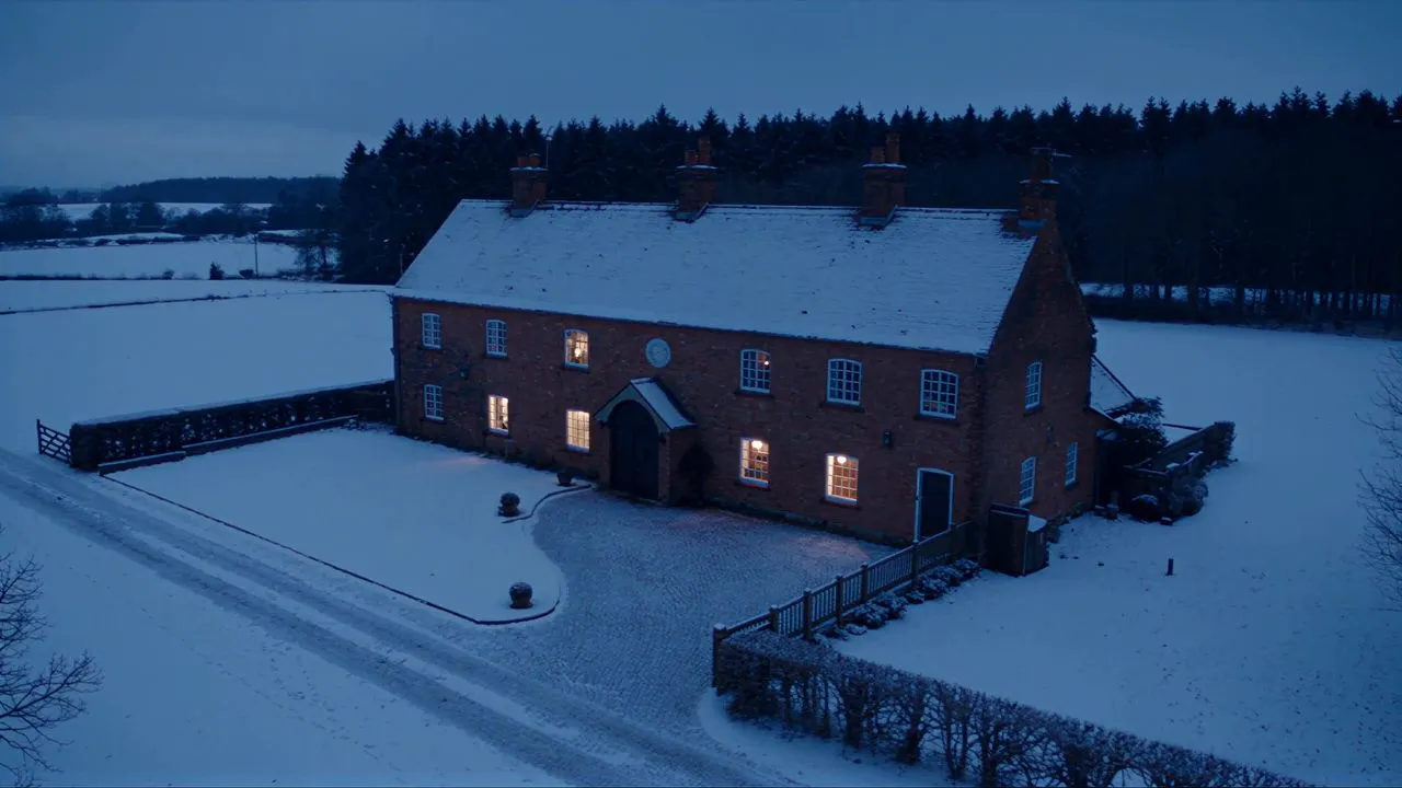 KI-generiertes Bild eines verschneiten Backsteinhauses am Abend aus der Luft, mit Hof, Zufahrt und Zaun im Schnee